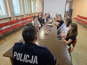 na zdjęciu policjant siedzi przy stole z ciastami z dziećmi