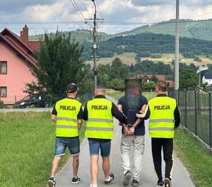 na zdjęciu policjanci w kamizelkach prowadzą zatrzymanego