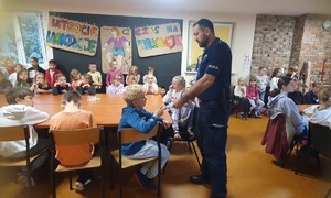 na zdjęciu policjant rozdaje ulotki dzieciom