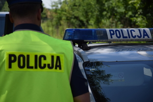 Zdjęcie przedstawia policjanta a w jego tle radiowóz
