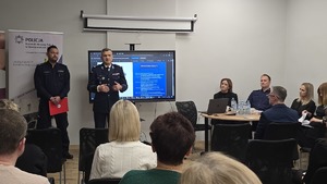 Zdjęcie przedstawia siedzących uczestników debaty oraz w drugim tle organizatorów i prowadzących debatę