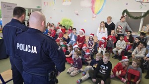 Na zdjęciu widnieje dwóch odwróconych plecami policjantów, którzy przemawiają do zebranych dzieci