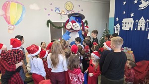 Zdjęcie przedstawia policyjną maskotkę Sznupka, który wita zgromadzone dzieci