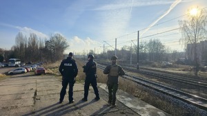Zdjęcie przedstawia trzech funkcjonariuszy - Policji, Straży Ochrony Kolei oraz żołnierza Wojska Polskiego na tle torowiska kolejowego