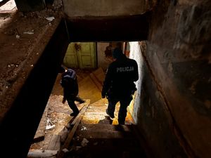 Zdjęcie przedstawia dwóch policjantów, którzy schodzą po schodach w opuszczonym budynku.