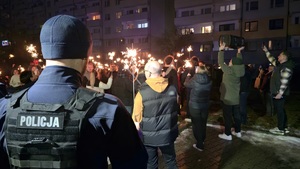 Na zdjęciu widać policjanta, a w jego tle kwestujących uczenistków symbolicznego światełka do nieba podczas Wielkiej Orkiestry Świątecznej Pomocy