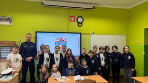 Zdjęcie przedstawia policjanta wraz z uczniami szkoły podstawowej, z którymi przeprowadzał prelekcję o bezpieczeństwie pieszych i rowerzystów