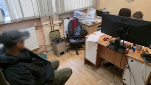 Na zdjęciu widoczny jest pokój, w którym przebywa zatrzymany mężczyzna wraz z policjantem.