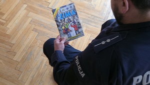 Zdjęcie przedstawia policjanta, trzymającego książeczkę na temat bezpieczeństwa zimą