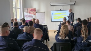 Zdjęcie przedstawia policjantów wraz z pracownikami miejskiego ośrodka pomocy społecznej, a w tle widoczny jest jeden z prowadzących zajęcia