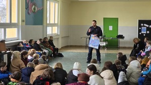 Na zdjęciu widnieje policjant tłumaczący zasady bezpieczeństwa dzieci na pierwszym tle