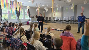 Zdjęcie przedstawia policjanta wraz z ratownikiem Wodnego Ochotniczego Pogotowia Ratunkowego, którzy promują bezpieczne zachowania zimą wśród zebranej młodzieży.