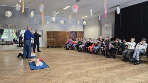Zdjęcie przedstawia policjanta wraz z ratownikiem Wodnego Ochotniczego Pogotowia Ratunkowego, którzy pokazują jak trzymać dłonie przy resuscytacji krążeniowo oddechowej