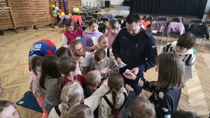 Na zdjęciu widać policjanta rozdającego dzieciom broszury informacyjne na temat bezpiecznych zachowań zimą