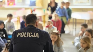 Zdjęcie przedstawia policyjnego profilaktyka, a w jego tle dzieci