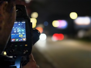 Zdjęcie przedstawia policjanta, który wykonuje pomiar ręcznym miernikiem prędkości