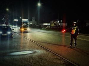 Na zdjęciu widoczny jest policjant, który zatrzymuje do kontroli kierującego pojazdem