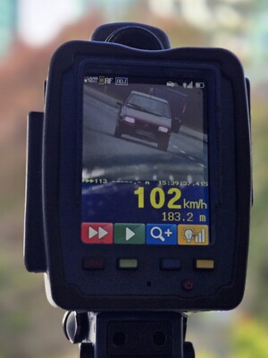 Zdjęcie przedstawia ręczny miernik prędkości na którym widoczne jest zdjęcie poruszającego się pojazdu po drodze.