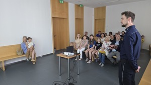 Na zdjęciu widoczny jest policjant, który prowadzi prezentację na temat cyberbezpieczeństwa. W tle zdjęcia widać widownię