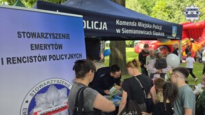 Zdjęcie przedstawia policyjne stanowisko profilaktyczne, gdzie znajduje się policjant, a dookoła zainteresowani ludzie
