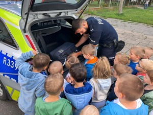 Na zdjęciu widoczny jest dzielnicowy w trakcie prezentacji dzieciom policyjnego radiowozu.