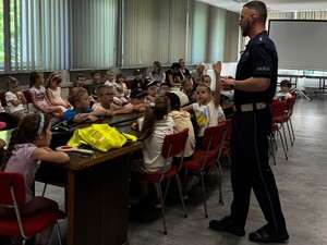 Na zdjęciu widoczny jest policjant drogówki, a w jego tle siedzące i przysłuchujące się mu dzieci