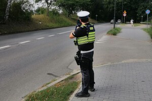 Na zdjęciu widoczny jest policjant ruchu drogowego, który stoi przy drodze i kontroluje
